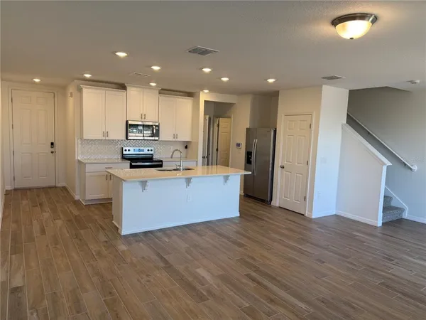 a large kitchen with stainless steel appliances a large counter top a stove and a wooden floors