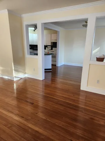 an empty room with wooden floor and a kitchen