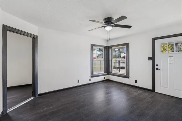 a view of an empty room with wooden floor and a ceiling fan