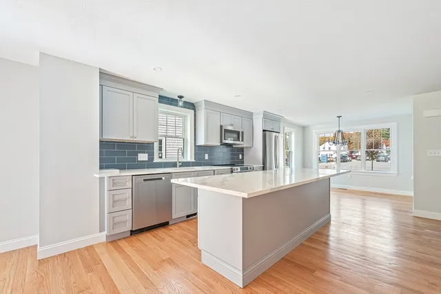 a large white kitchen with kitchen island a sink wooden floor and stainless steel appliances