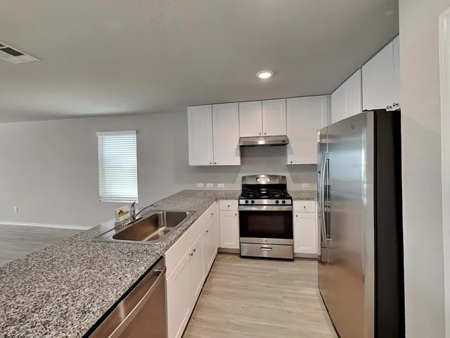 a view of a kitchen with kitchen island a sink wooden floor and black appliances