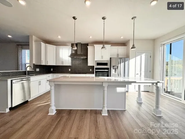 a open kitchen with stainless steel appliances granite countertop a stove a sink a center island a refrigerator and a wooden floor