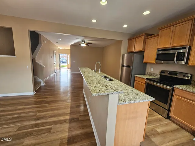 a kitchen with stainless steel appliances kitchen island granite countertop a refrigerator a stove and a sink with wooden floor