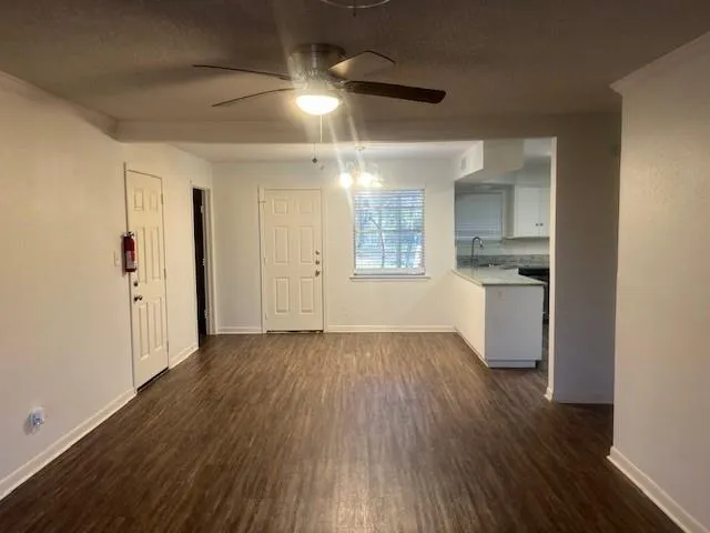 an empty room with wooden floor and a kitchen