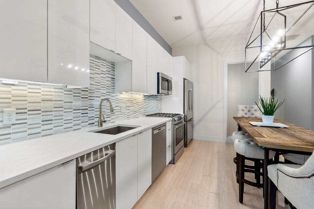 121 Portland Street, Unit 206 Boston, MA 02114 - Photo 8 of 35 a kitchen with stainless steel appliances kitchen island a table chairs in it and wooden floors