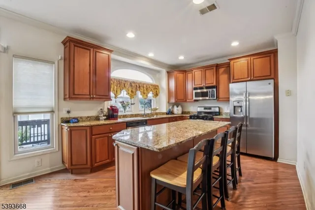 a kitchen with stainless steel appliances granite countertop a stove top oven a refrigerator a sink and a dining table with wooden floor