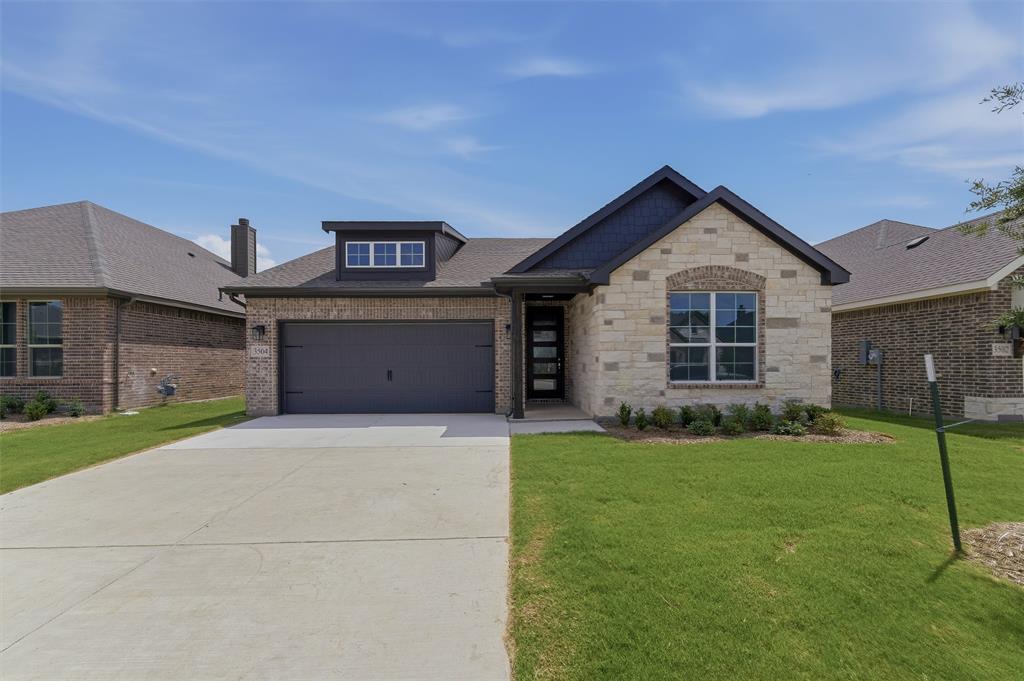 3504 Helena Street Gainesville, TX 76240 - Photo 3 of 19 Modern single-story residence featuring a combination brick and stone exterior, a dark gray garage door, and a dormer with multiple windows