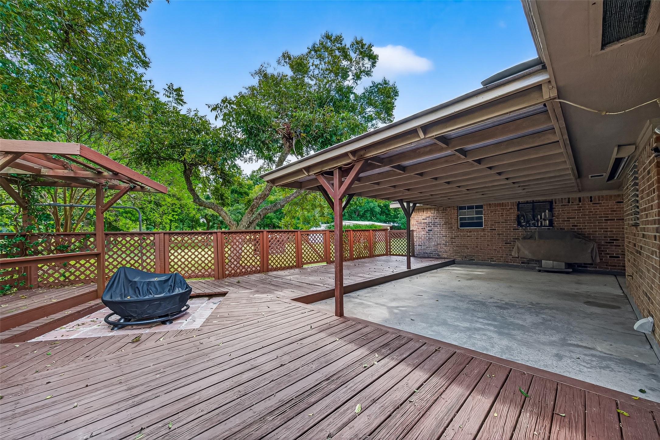 12021 7th 1/2 Street Santa Fe, TX 77510 - Photo 10 of 49 This photo shows a spacious backyard patio featuring a large wooden deck with a fire pit and a covered area for shade and ready for hot tub to be installed. The space is surrounded by lush greenery, providing a private and serene outdoor setting. Perfect for entertaining or relaxing.