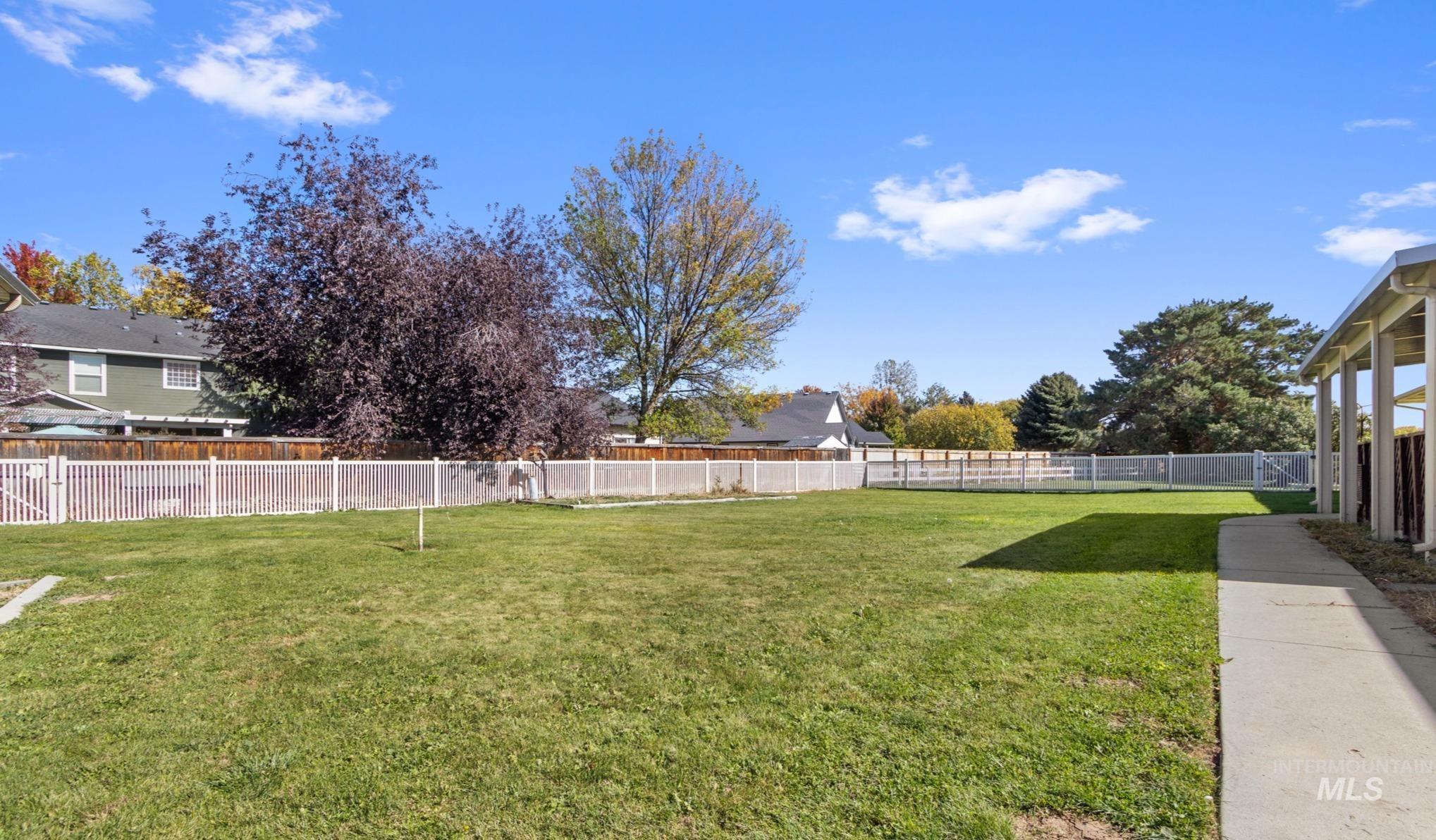 11360 West Lake Hazel Road Boise, ID 83709 - Photo 47 of 50 Expansive lawn area with a chain-link perimeter fence, brick exterior, covered patio, and mature landscaping