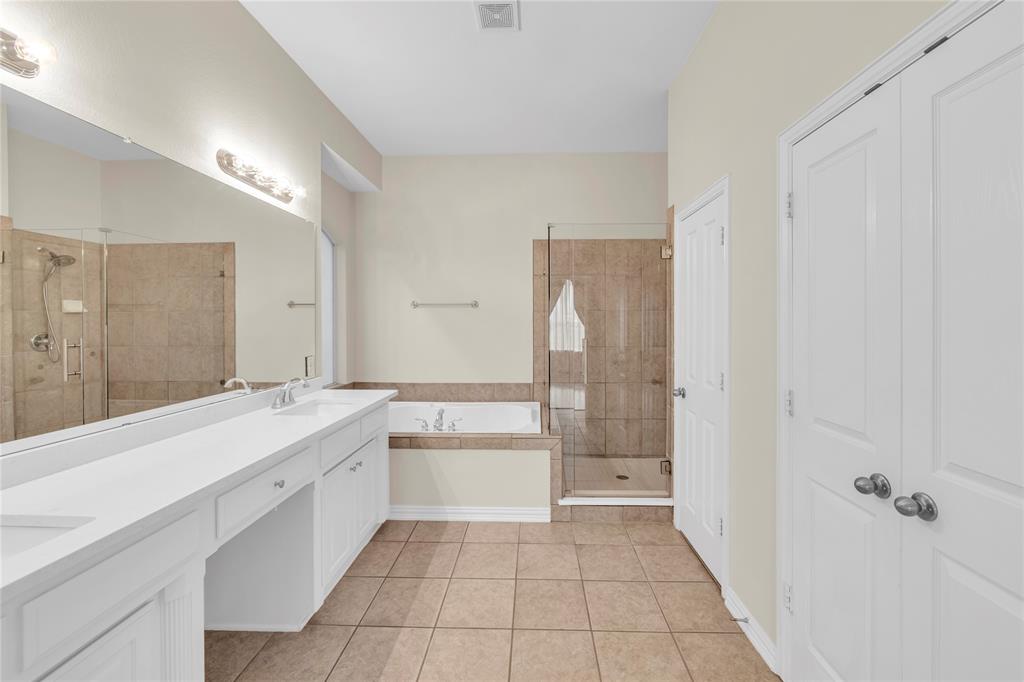 3920 Autumn Lane Bedford, TX 76021 - Photo 22 of 36 Bathroom featuring a dual vanity with white cabinetry and countertop, a large frameless mirror, a built-in tub with tile surround, a glass-enclosed shower with tile walls, and tiled flooring