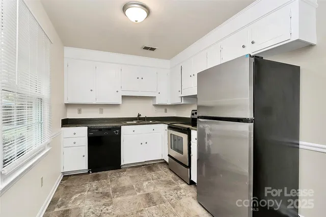 a kitchen with granite countertop a refrigerator stove and white cabinets