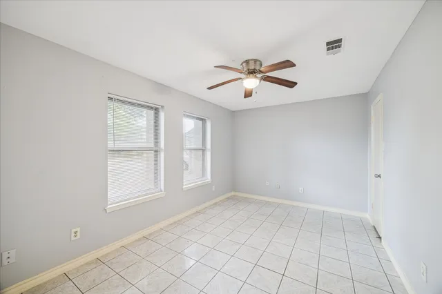 an empty room with chandelier fan and windows