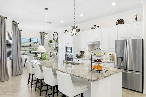 a kitchen with stainless steel appliances kitchen island granite countertop a refrigerator a oven a sink and a chandelier