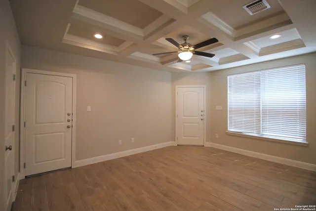an empty room with wooden floor ceiling fan and windows