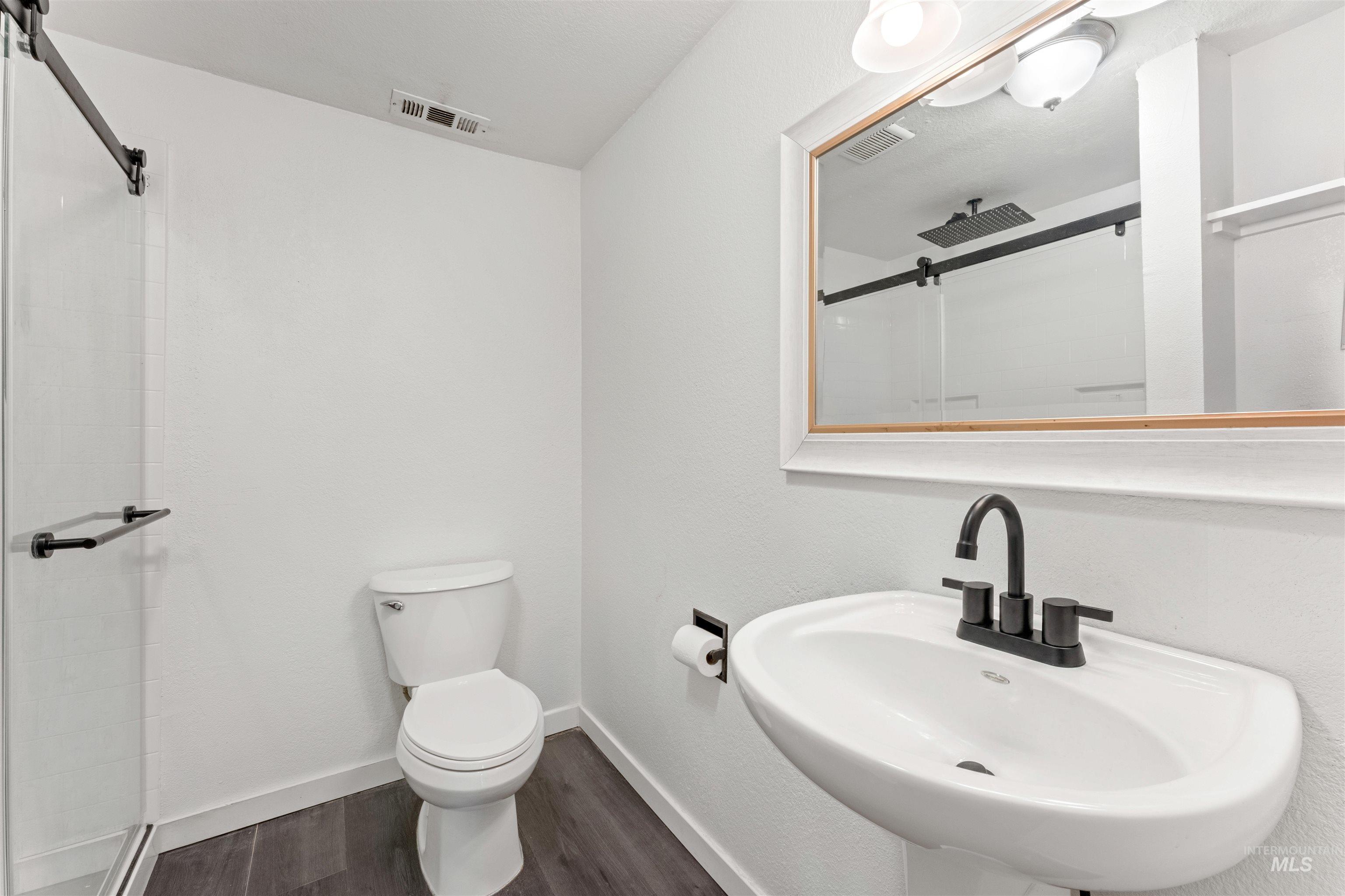 17441 Upper Pleasant Ridge Road Caldwell, ID 83607 - Photo 26 of 40 Contemporary bathroom featuring a pedestal sink with a matte black faucet, a white framed mirror, and wood-finish flooring
