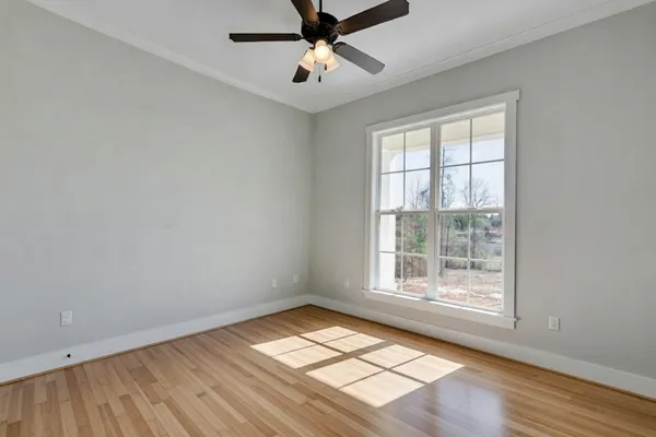 an empty room with wooden floor chandelier fan and windows