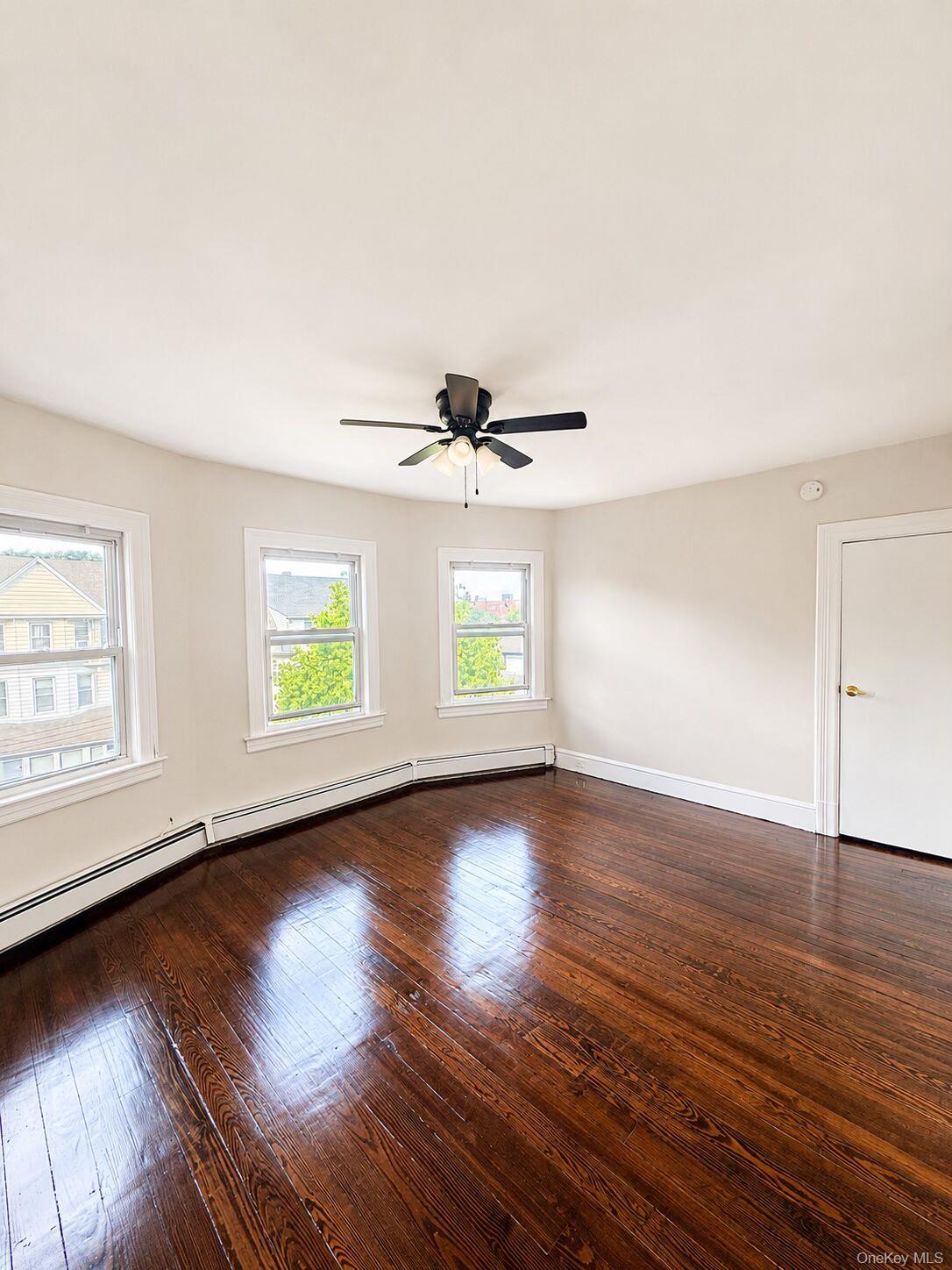 79 Division Street, Unit 3 New Rochelle, NY 10805 - Photo 4 of 17 Spacious room with dark wood-finish flooring, multiple windows, and a ceiling fan with integrated lighting.