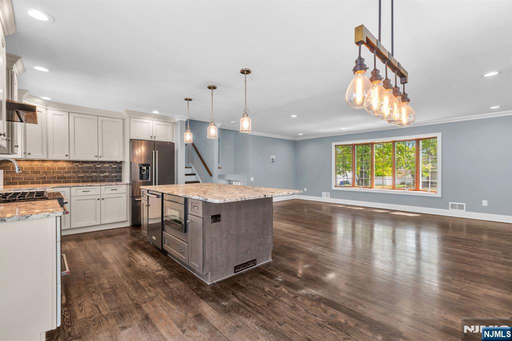 53 Smithfield Road Waldwick, NJ 07463 - Photo 19 of 48 a kitchen with kitchen island granite countertop a stove a sink a refrigerator and a dining table with wooden floor
