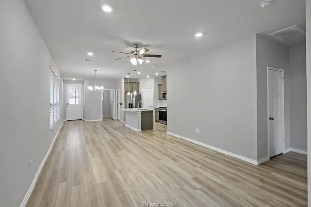 a view of an empty room and kitchen view with wooden floor