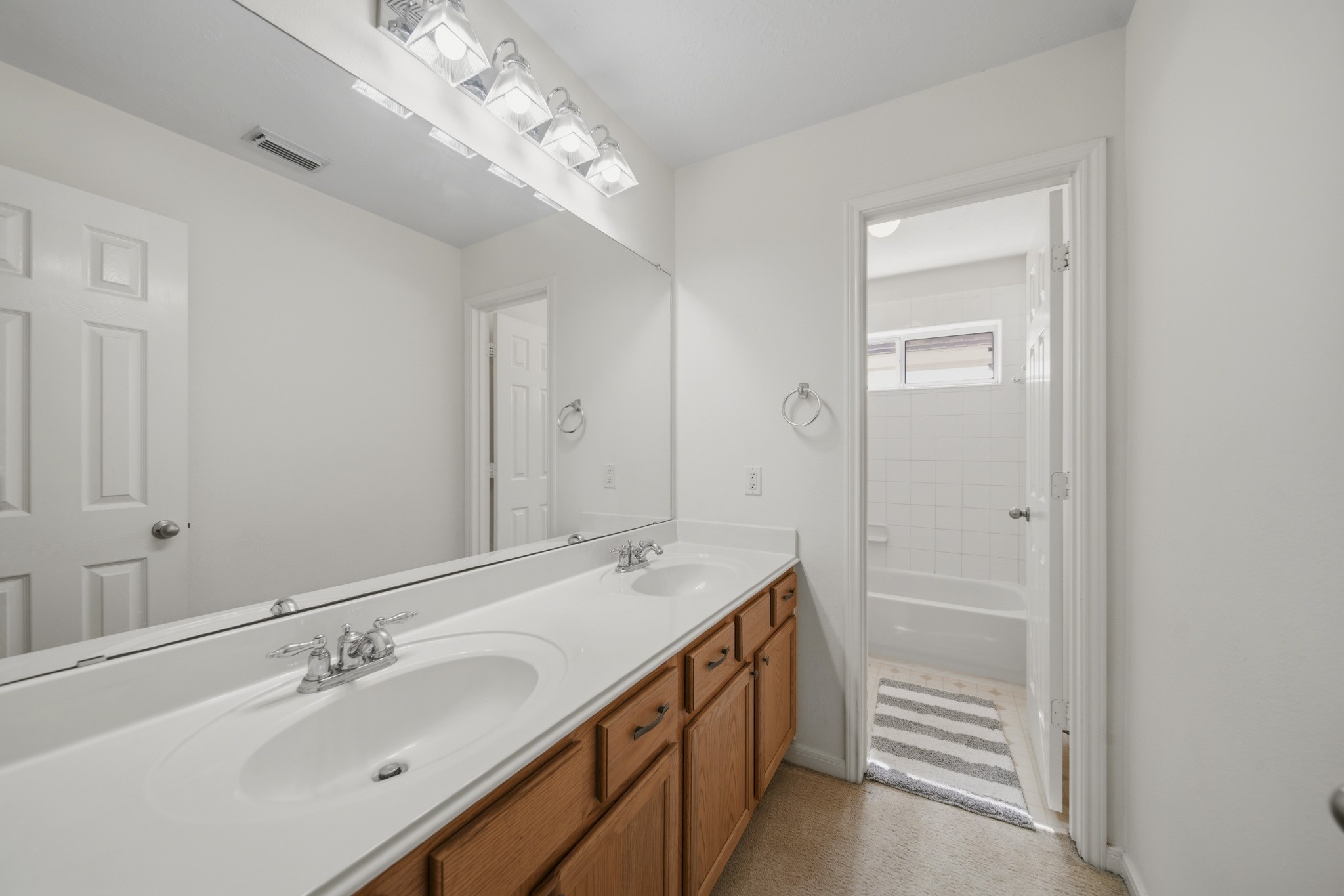3306 Colleville Sur Mer Lane Spring, TX 77388 - Photo 18 of 30 This well-appointed secondary bathroom offers a functional and family-friendly layout with a spacious dual-sink vanity and an expansive countertop, providing plenty of room for daily routines. A large wall-to-wall mirror enhances the sense of space while reflecting light throughout the room. The bathroom features a private tub and shower area, creating added convenience and privacy for shared use.