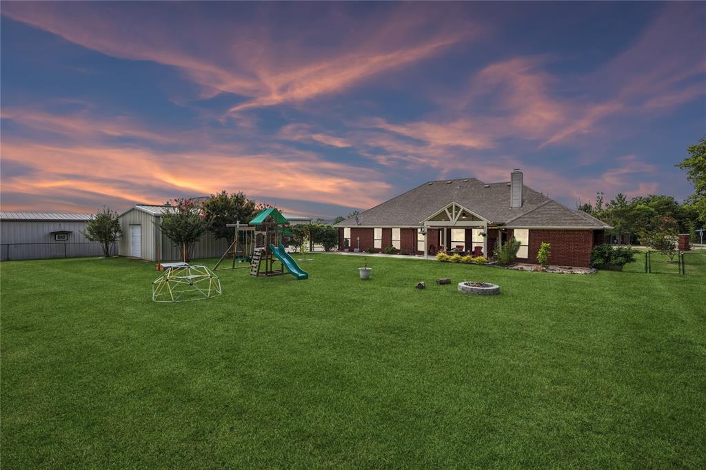 11211 Emerald Ranch Lane Forney, TX 75126 - Photo 3 of 35 Expansive rear yard featuring a manicured lawn, brick exterior residence, covered patio, and a detached shed