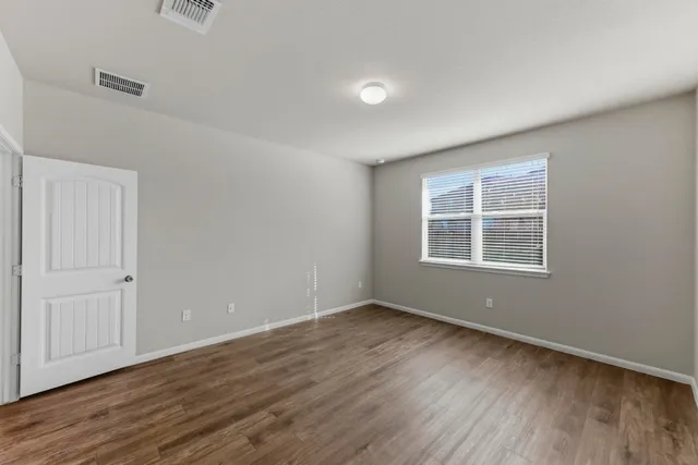 a view of an empty room with wooden floor and a window