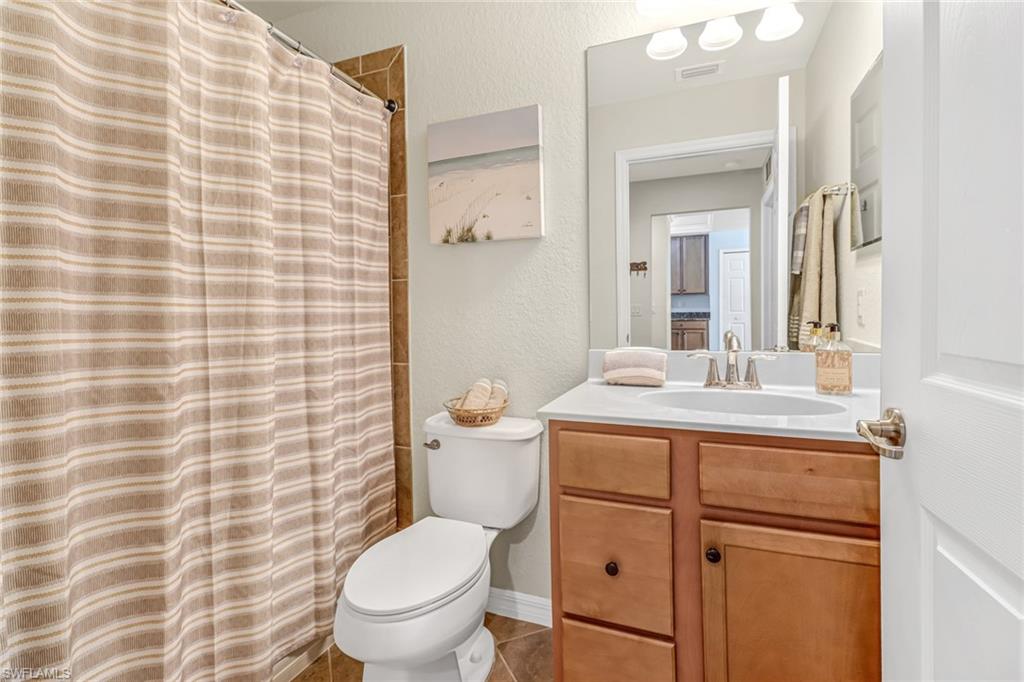 9521 Avellino Way, Unit 2415 Naples, FL 34113 - Photo 40 of 48 a bathroom with a granite countertop toilet a sink a mirror and a shower
