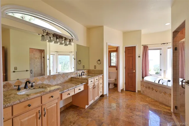 a spacious bathroom with a granite countertop double vanity sink a mirror and a bathtub