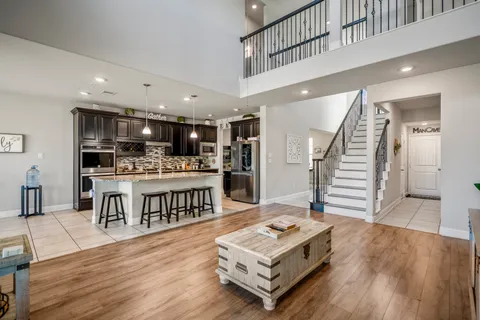 a living room with stainless steel appliances kitchen island granite countertop a refrigerator a stove a sink dishwasher and a dining table with wooden floor