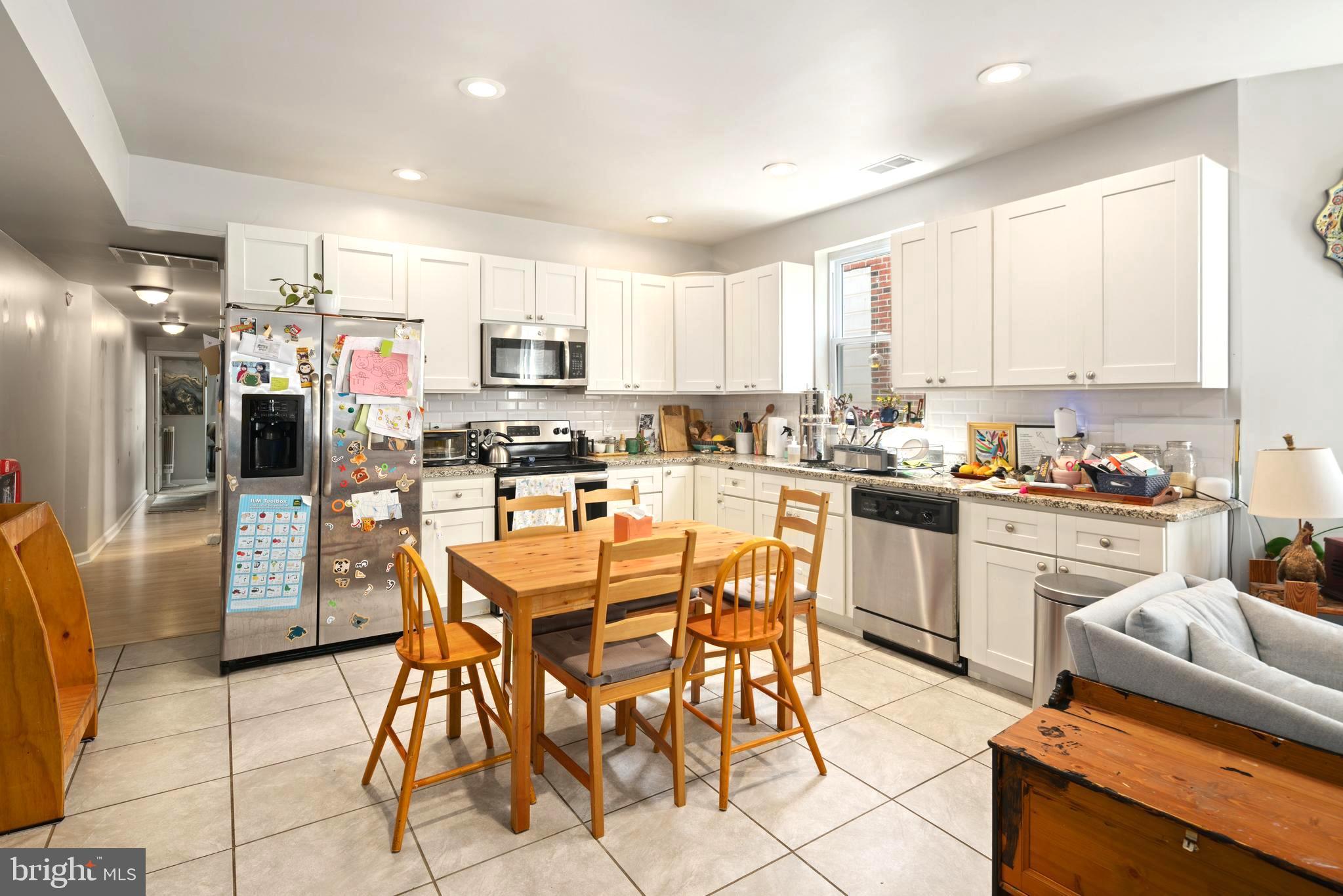 4804 Kingsessing Avenue Philadelphia, PA 19143 - Photo 7 of 17 a kitchen with stainless steel appliances kitchen island granite countertop a stove a refrigerator a stove a dining table and chairs with white cabinets