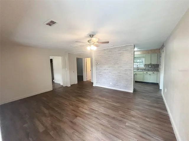 a view of empty room with wooden floor and kitchen view