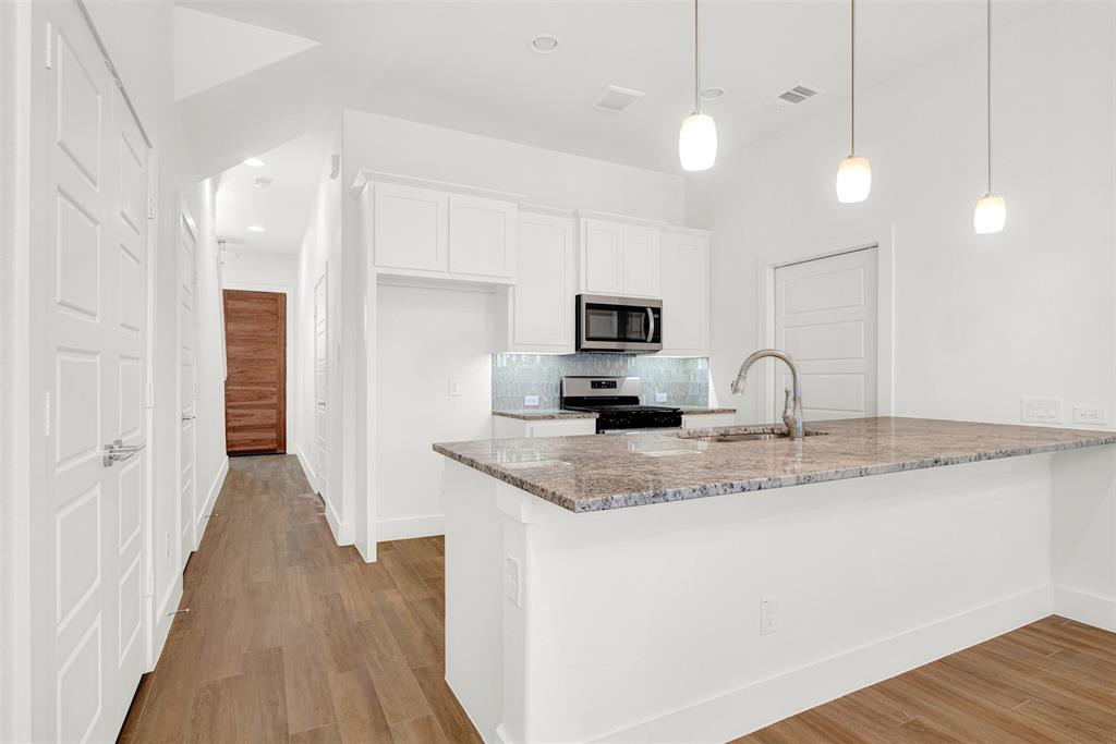 3676 Rickshaw Drive, Unit D Dallas, TX 75229 - Photo 3 of 22 a kitchen with stainless steel appliances granite countertop a sink a microwave oven a refrigerator with white cabinets and wooden floor