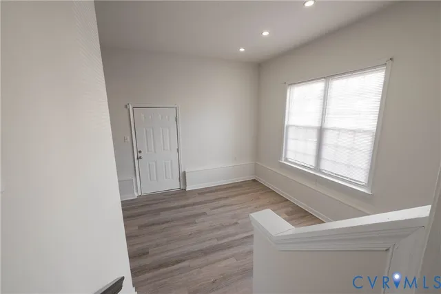 a view of an empty room with wooden floor and a ceiling fan