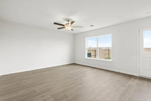 an empty room with wooden floor fan and windows
