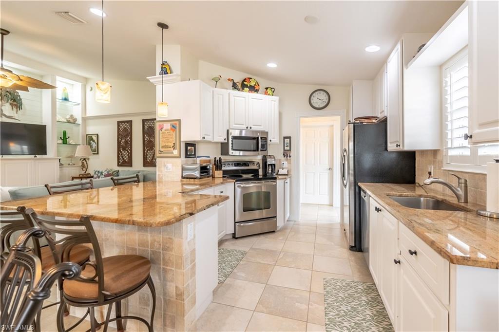 7568 Novara Court Naples, FL 34114 - Photo 15 of 34 a large kitchen with stainless steel appliances kitchen island granite countertop a sink and cabinets