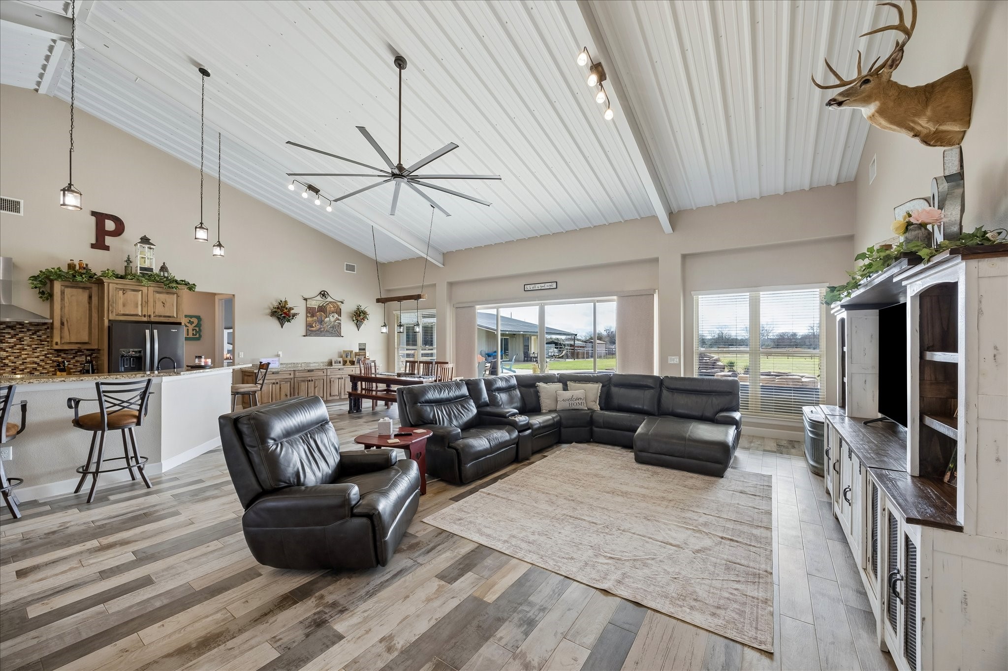 2224 Maler Road Sealy, TX 77474 - Photo 12 of 50 This spacious open-concept living area features high vaulted ceilings, a modern ceiling fan, and large windows providing plenty of natural light. The dining area offers ample space for gatherings, and the room has a warm, inviting atmosphere with views of the outdoors.