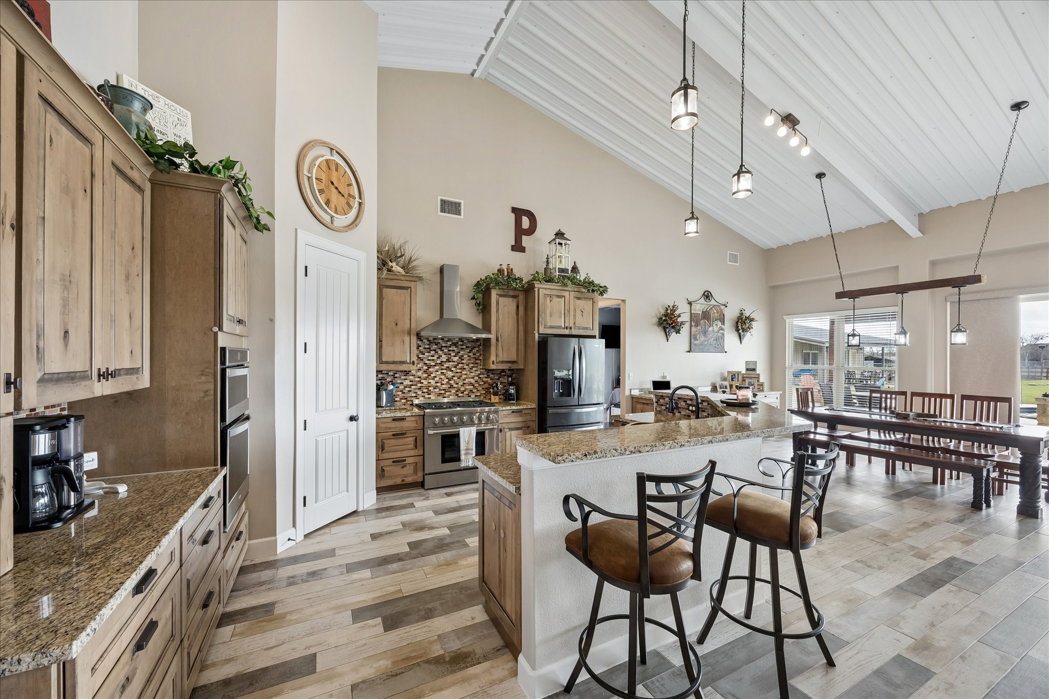 2224 Maler Road Sealy, TX 77474 - Photo 15 of 50 This spacious kitchen features rustic wooden cabinets, granite countertops, and a central island with bar seating. The high vaulted ceiling and large windows enhance the airy feel, while pendant lighting adds elegance.