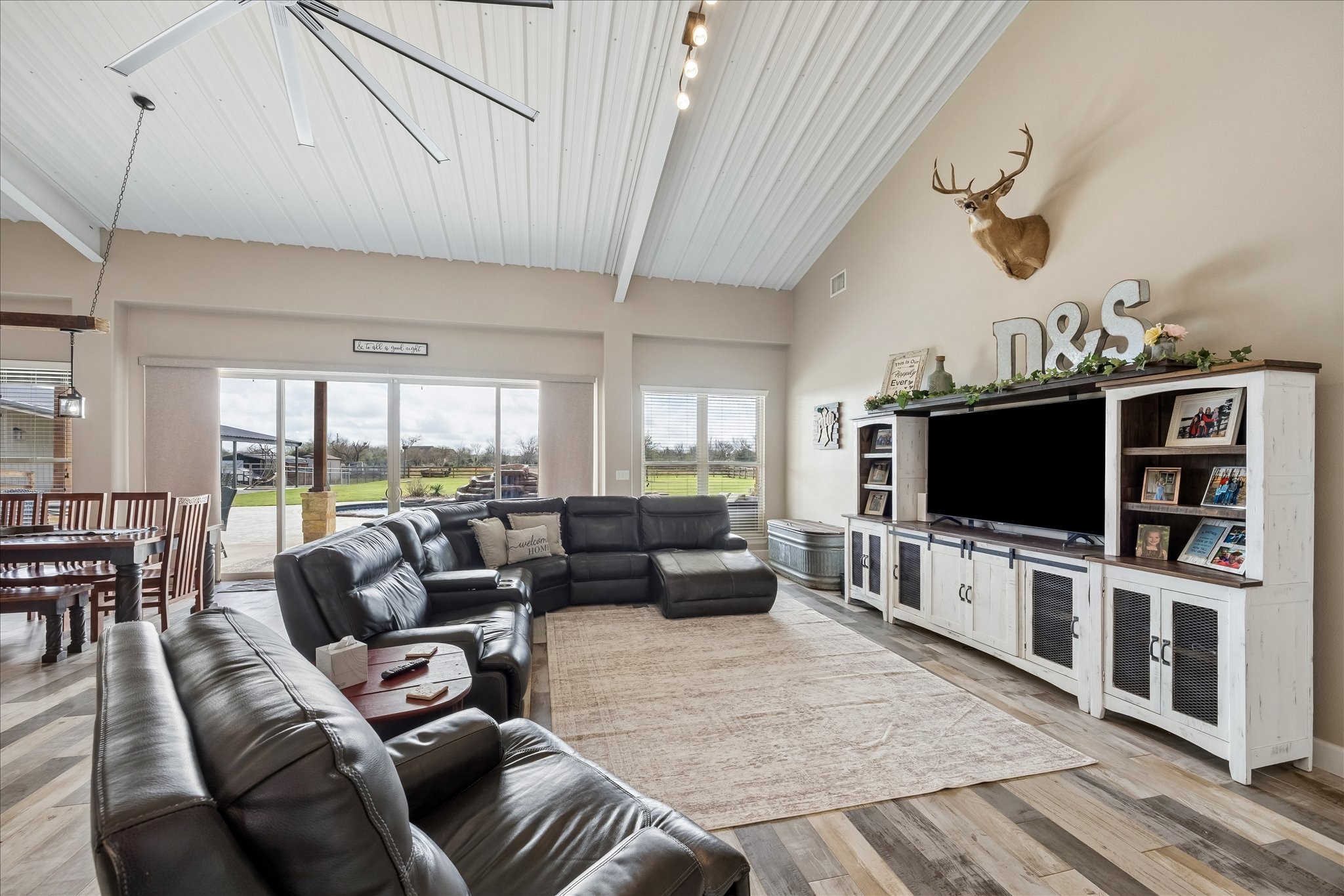 2224 Maler Road Sealy, TX 77474 - Photo 5 of 50 This spacious living room features high ceilings with a modern fan, large windows offering natural light and beautiful views. The room connects to a dining area, creating an open and inviting space perfect for family gatherings.