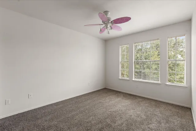 an empty room with a chandelier fan and windows