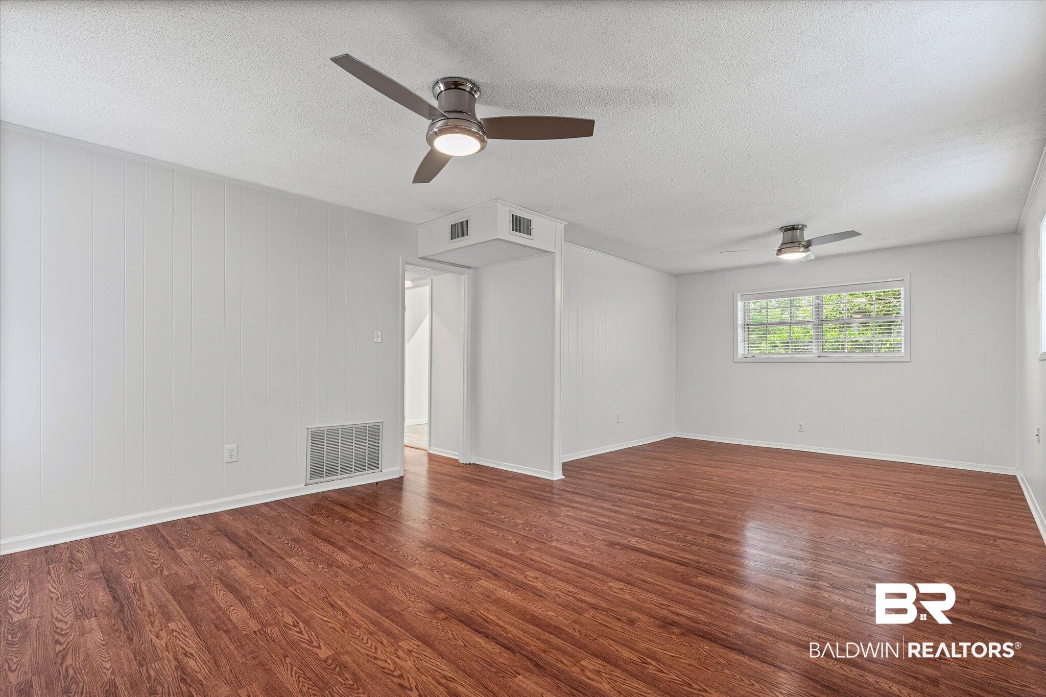 8301 Fordham Road Mobile, AL 36619 - Photo 23 of 57 Spacious room featuring wood-finish flooring, white paneled walls, and two ceiling fans with integrated lighting