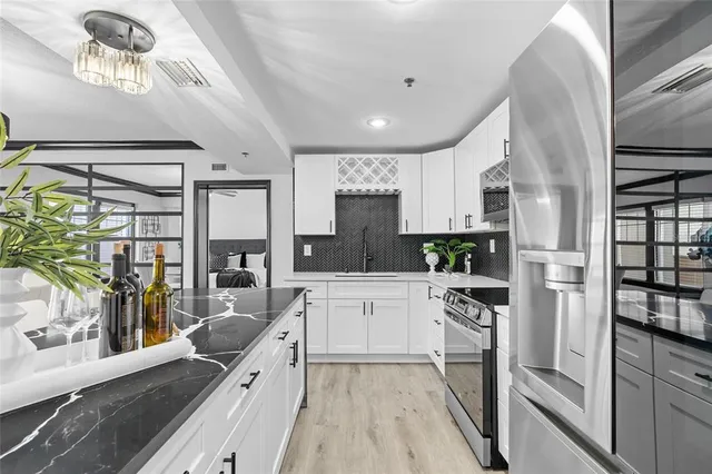 a kitchen with stainless steel appliances granite countertop a refrigerator a stove a sink dishwasher and white cabinets with wooden floor