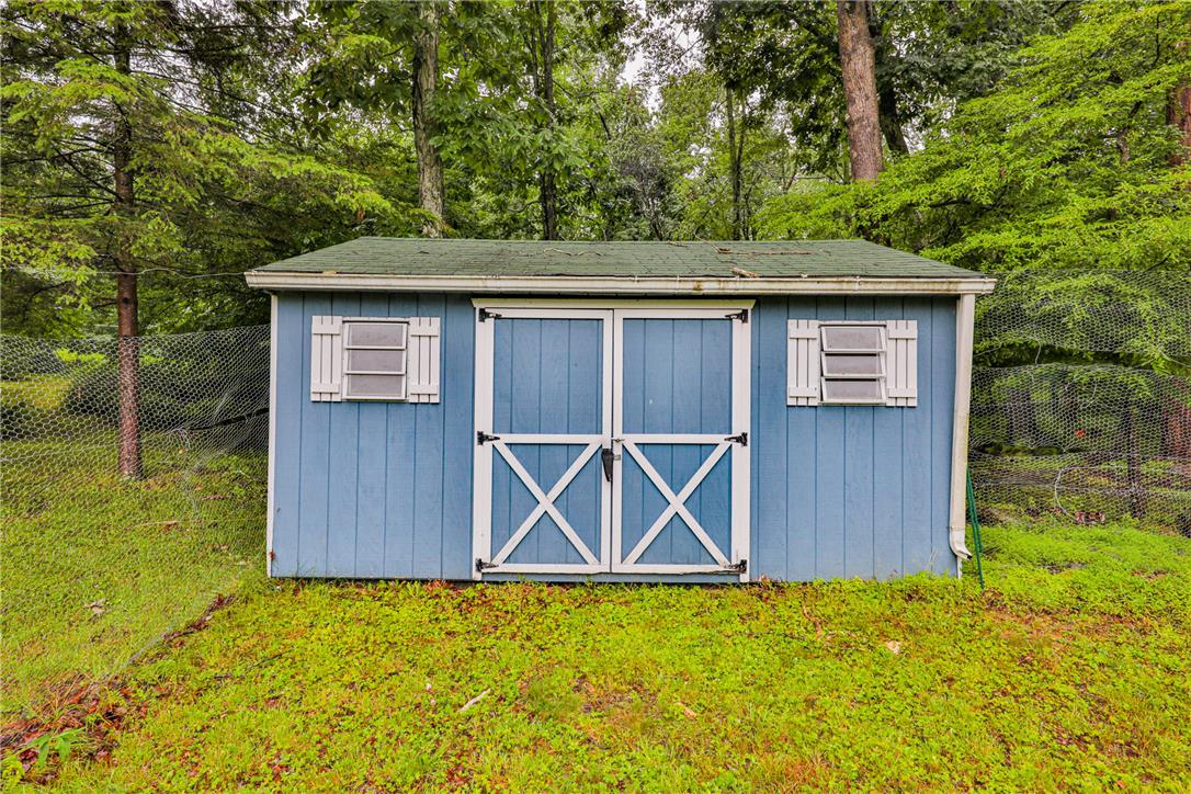5599 Minks Pond Road Bushkill, PA 18324 - Photo 63 of 64 A quaint blue storage shed with charming white trim nestled amongst lush trees, offering functional outdoor space.