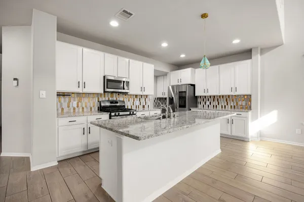 a kitchen with stainless steel appliances granite countertop a stove top oven a sink and white cabinets