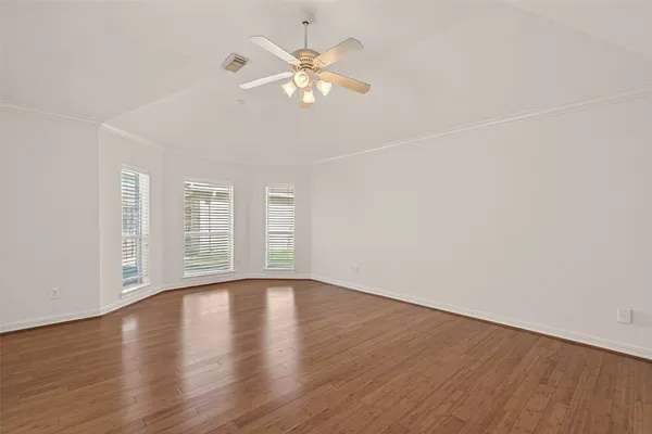 an empty room with wooden floor fan and windows