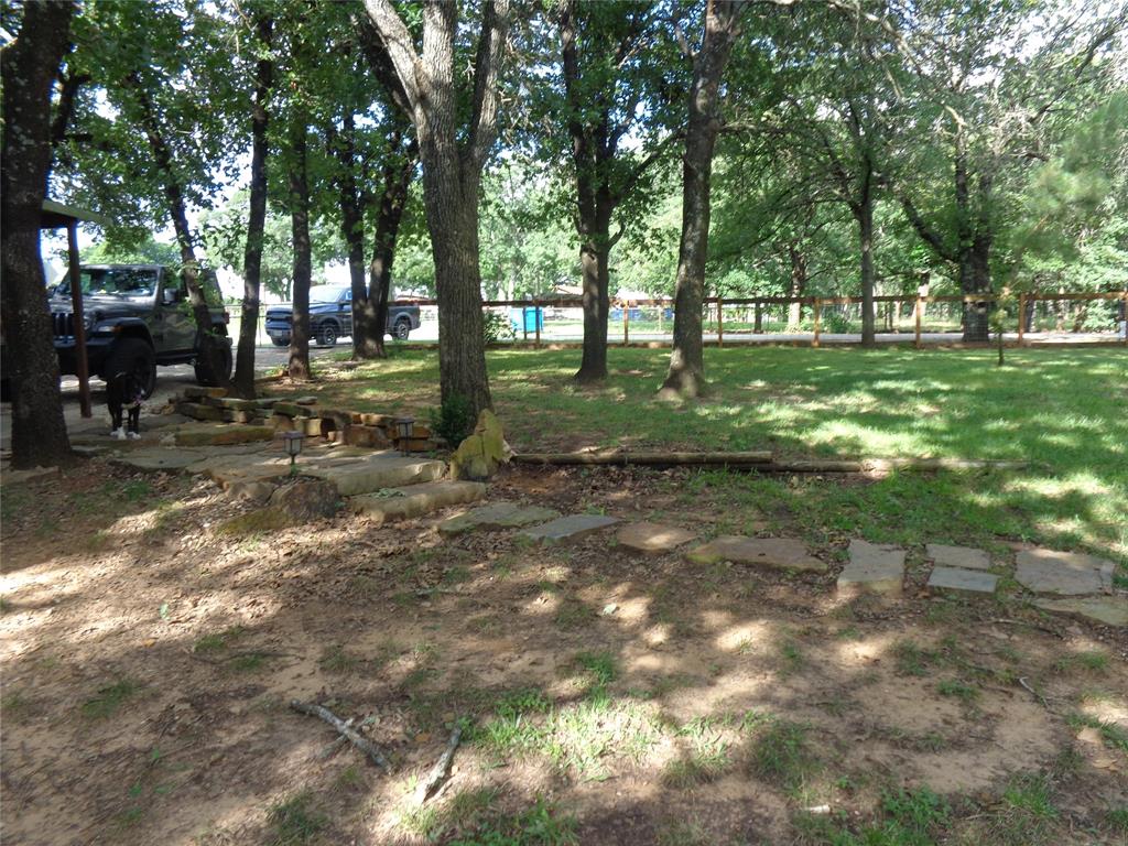 5525 Cedar Oaks Road Grandview, TX 76050 - Photo 28 of 40 Expansive outdoor area featuring mature trees providing shade, a natural stone pathway, and a grassy expanse bordered by a wooden fence