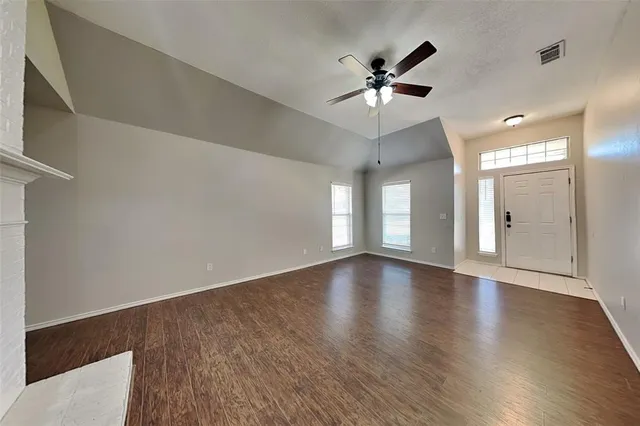 a view of an empty room with wooden floor and a ceiling fan