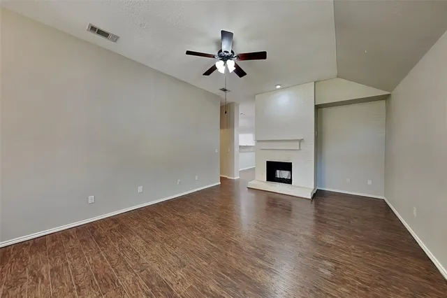 a view of an empty room with wooden floor a fireplace and a window