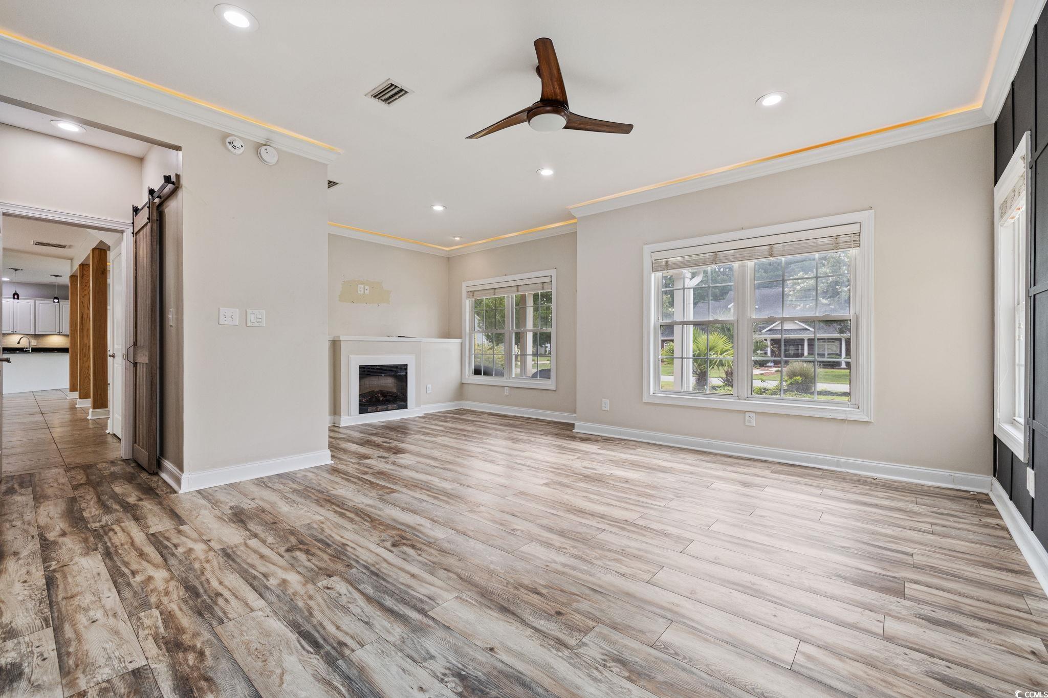 11569 Bay Drive Little River, SC 29566 - Photo 15 of 40 Unfurnished living room featuring a barn door, a ceiling fan, ornamental molding, wood finished floors, and a fireplace
