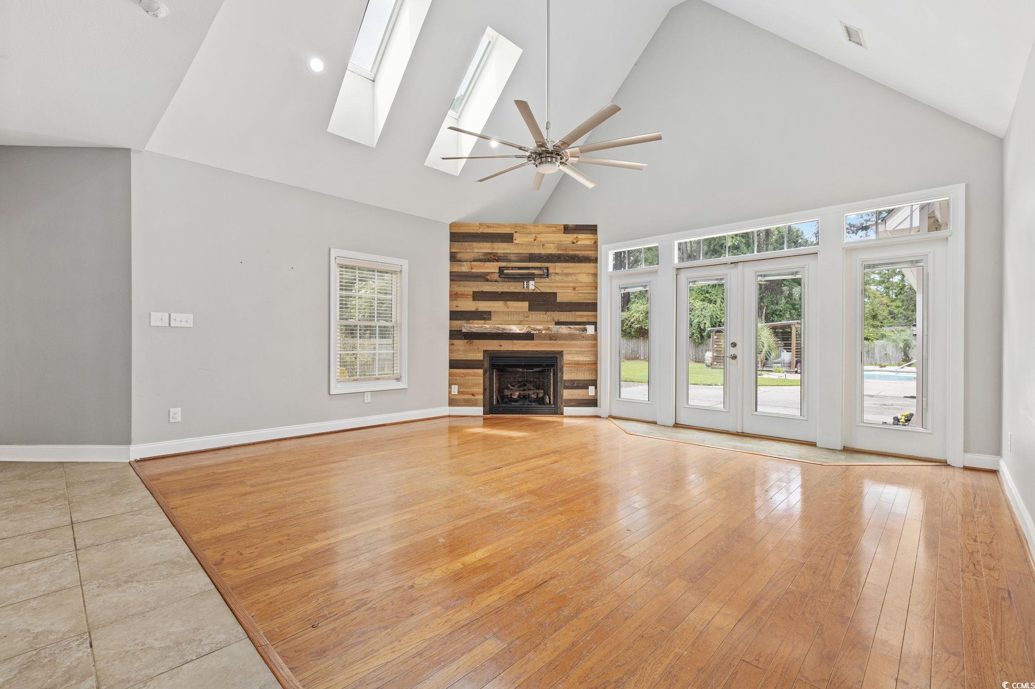 11569 Bay Drive Little River, SC 29566 - Photo 7 of 40 Unfurnished living room with light wood-type flooring, high vaulted ceiling, a fireplace, ceiling fan, and a skylight
