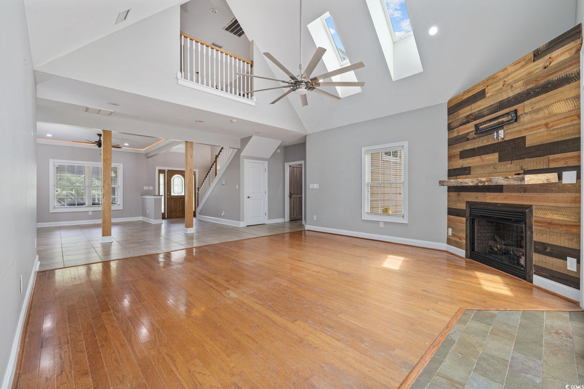 11569 Bay Drive Little River, SC 29566 - Photo 8 of 40 Unfurnished living room with a ceiling fan, hardwood / wood-style floors, a tile fireplace, a skylight, and lofted ceiling